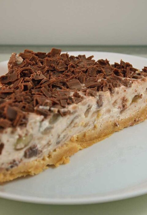 Een stuk banaan kwarktaart met chocolade op een wit bord.