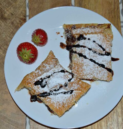 Bananenflaps met chocoladepasta en aardbei op een wit bordje met 2 verse aardbeiden.