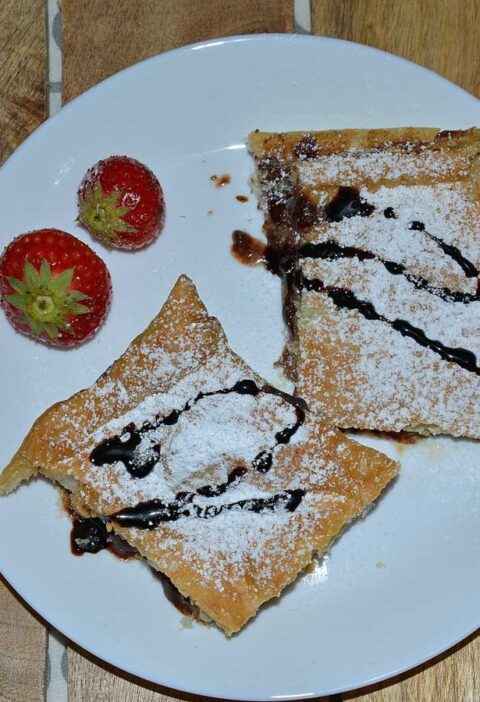 Bananenflaps met chocoladepasta en aardbei op een wit bordje met 2 verse aardbeiden.