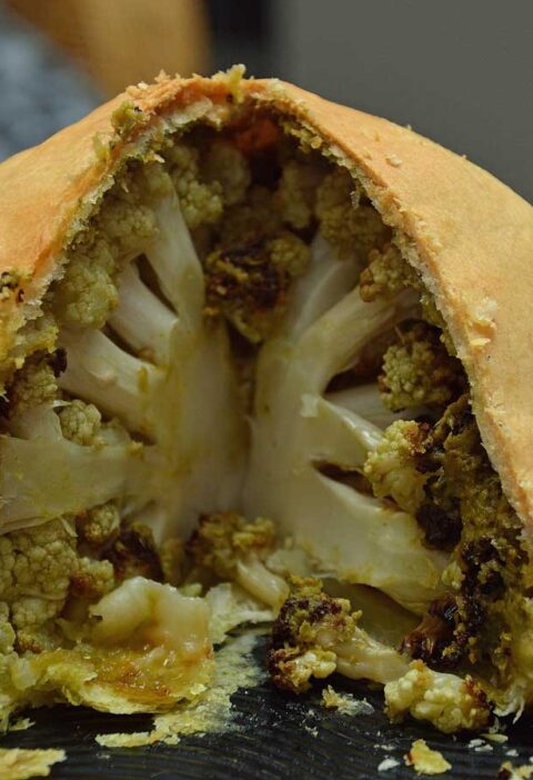 Hele bloemkool met pesto in bladerdeeg op een platte schaal.