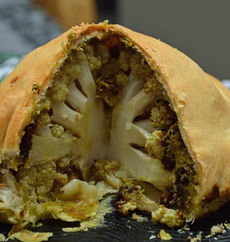 Hele bloemkool met pesto in bladerdeeg op een platte schaal.