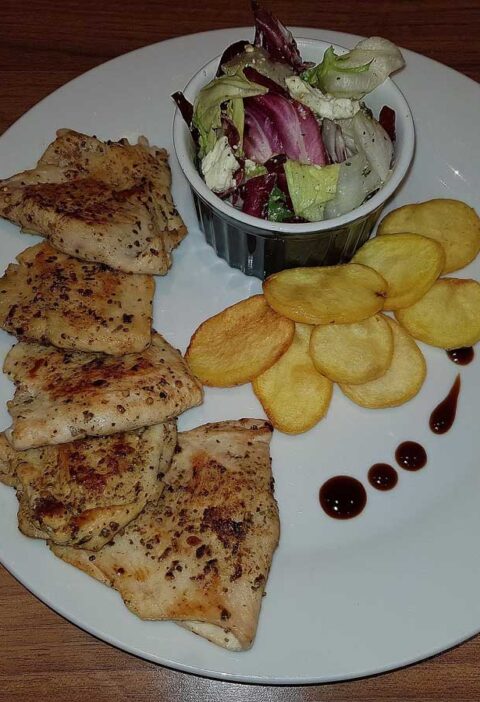 Gevulde kipschnitzel met feta, naast een salade en gefrituurde aardappelschijfjes.