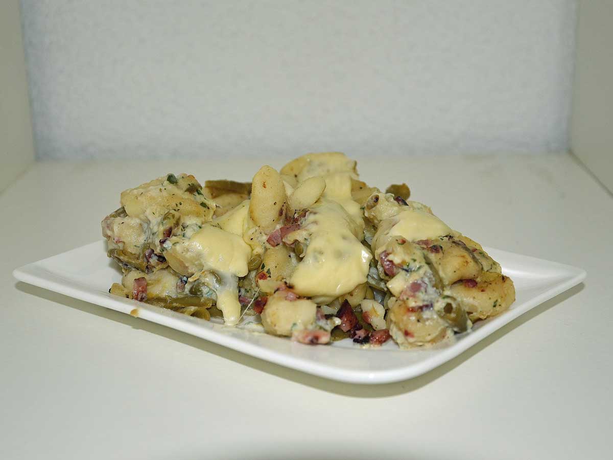 Gnocchi carbonara met bonen op een rechthoekig wit bordje.