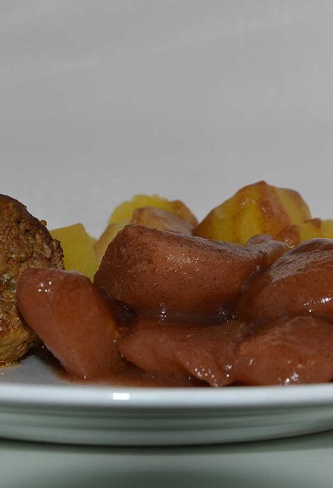 Een bord met stoofpeertjes met gekookte aardappelen en een gehaktbal.