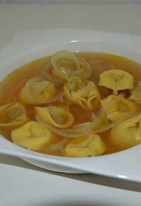 Een soepbord met uiensoep met tortellini.
