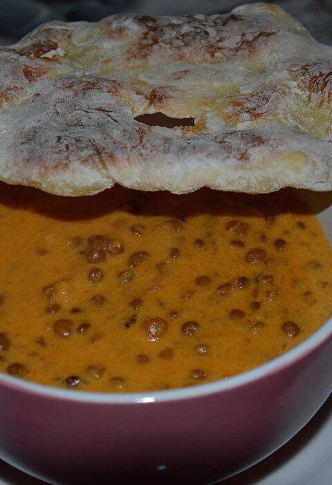 Een soepkom met wortel linzensoep en een stuk naanbrood er bovenop.