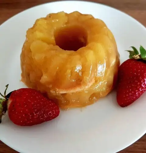 Een appel-vanille taartje op een wit bordje met 2 verse aardabeien.