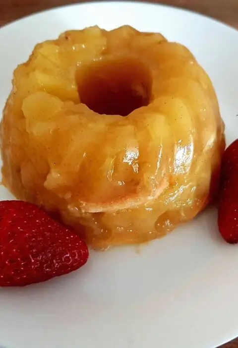 Een appel-vanille taartje op een wit bordje met 2 verse aardabeien.