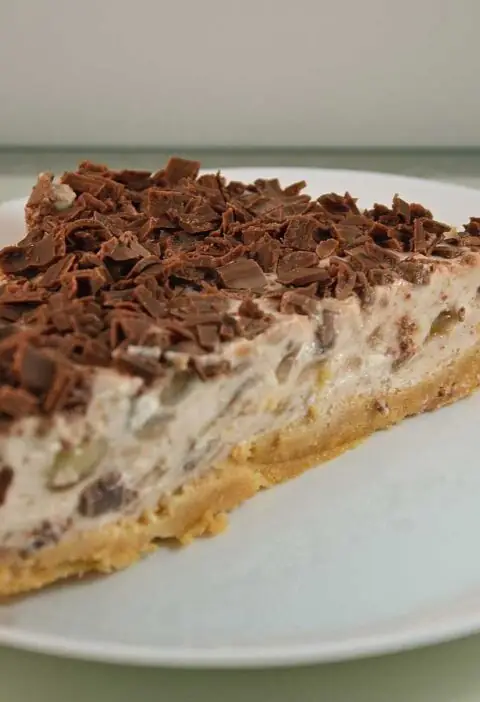Een stuk banaan kwarktaart met chocolade op een wit bord.