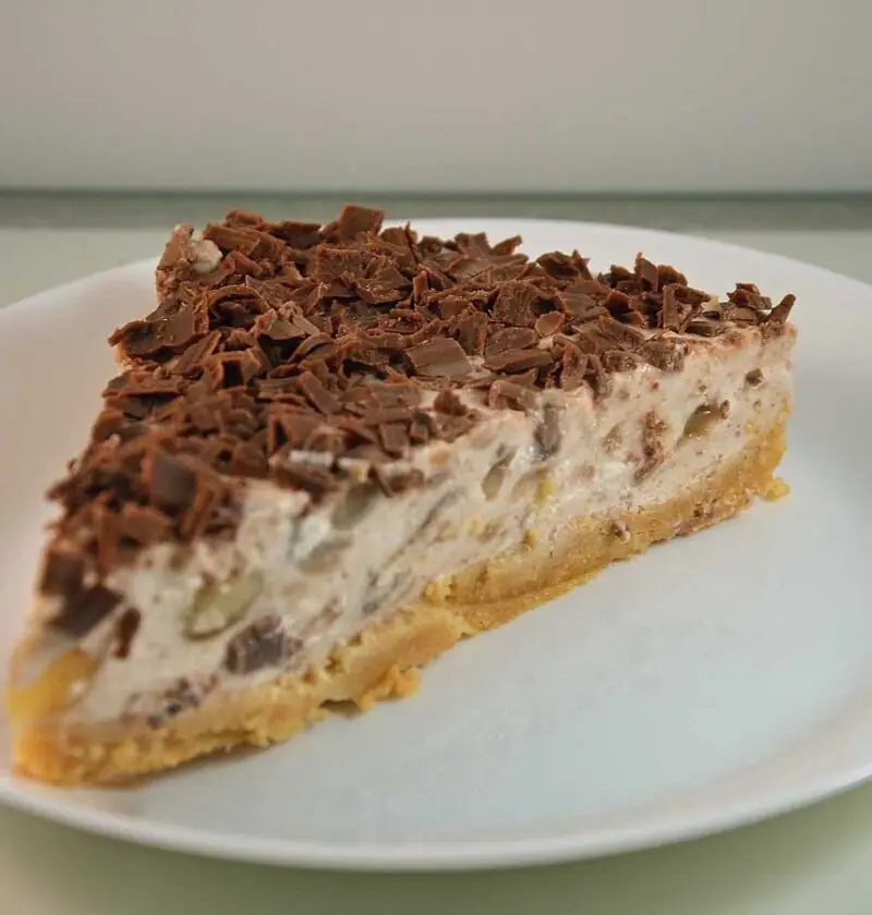 Een stuk banaan kwarktaart met chocolade op een wit bord.
