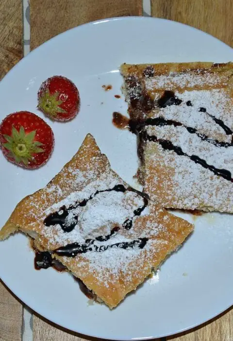 Bananenflaps met chocoladepasta en aardbei op een wit bordje met 2 verse aardbeiden.