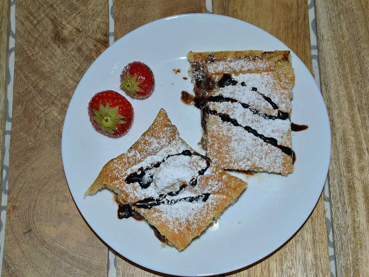 Bananenflaps met chocoladepasta en aardbei op een wit bordje met 2 verse aardbeiden.