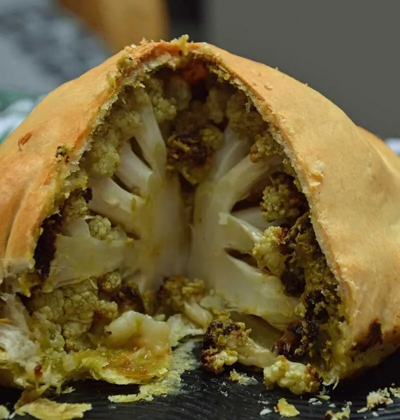 Hele bloemkool met pesto in bladerdeeg op een platte schaal.
