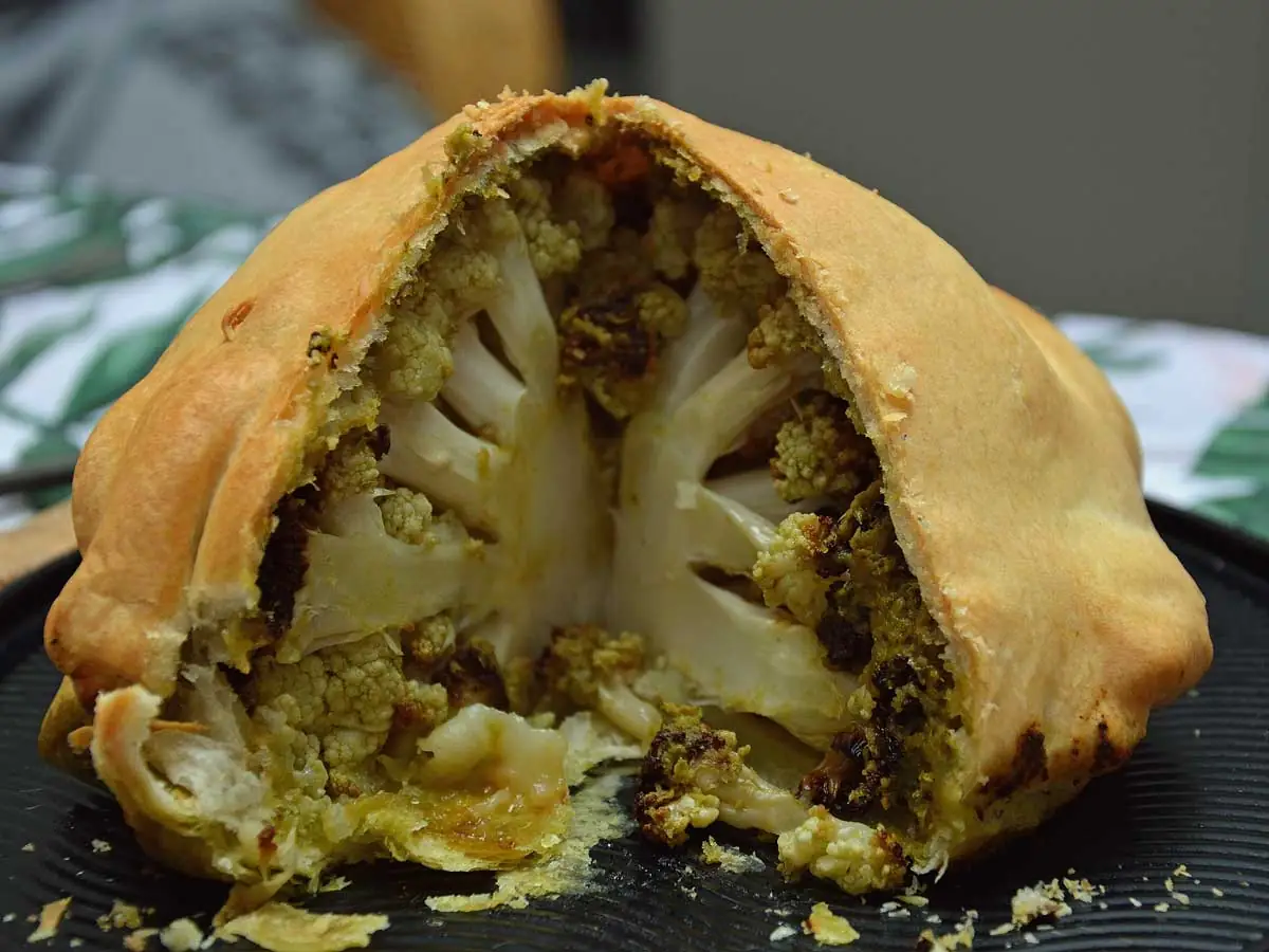 Hele bloemkool met pesto in bladerdeeg op een platte schaal.