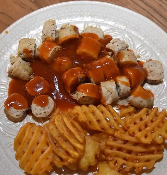 Een bord met zelfgemaakte Duitse curryworst en wafelpatat uit de aanbieding.