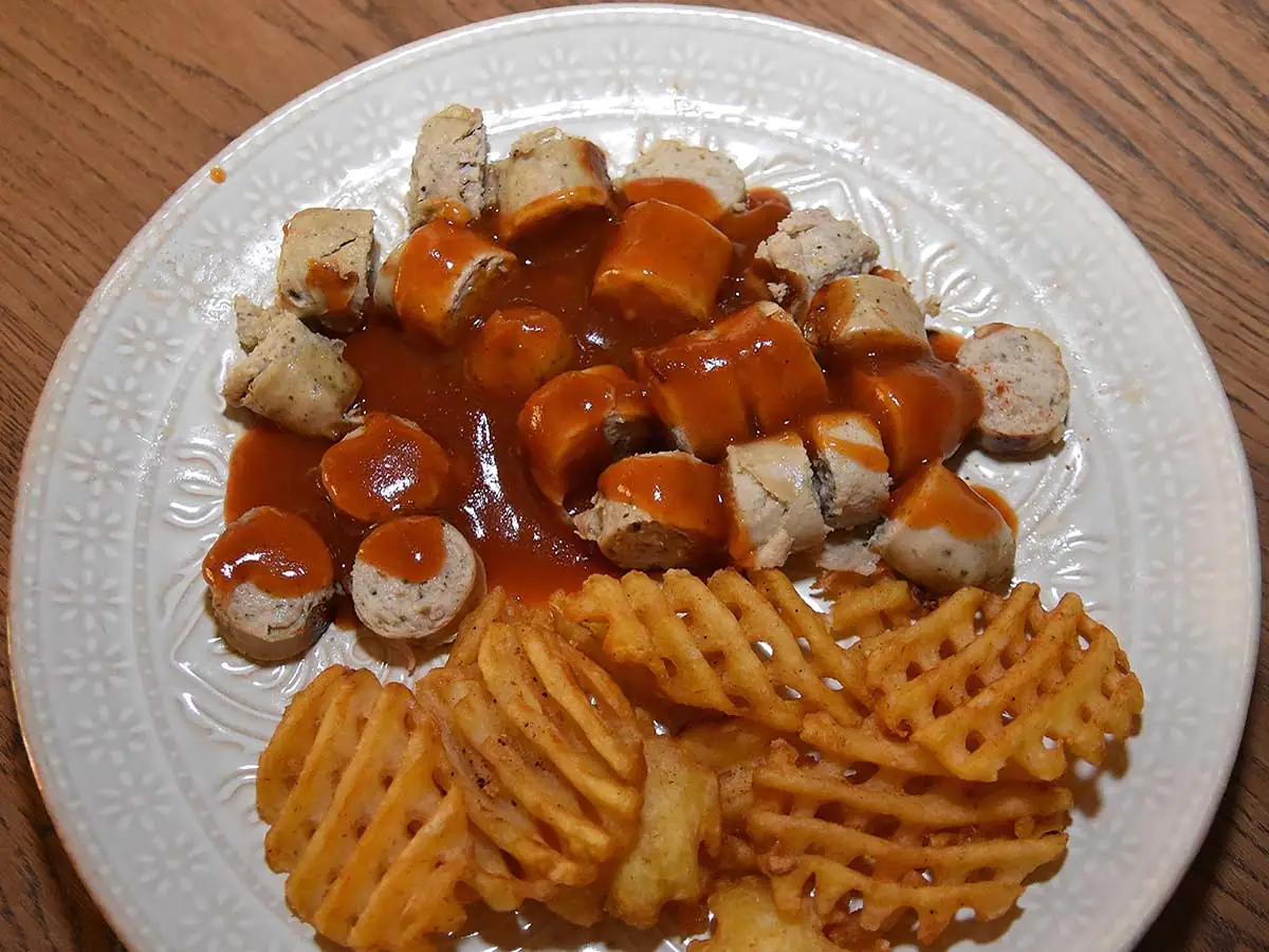 Een bord met zelfgemaakte Duitse curryworst en wafelpatat uit de aanbieding.