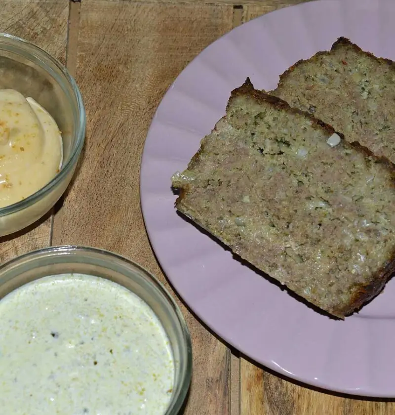 2 plakken gehaktbrood pesto met basilicumsaus op een paars bordje. met sauzen.