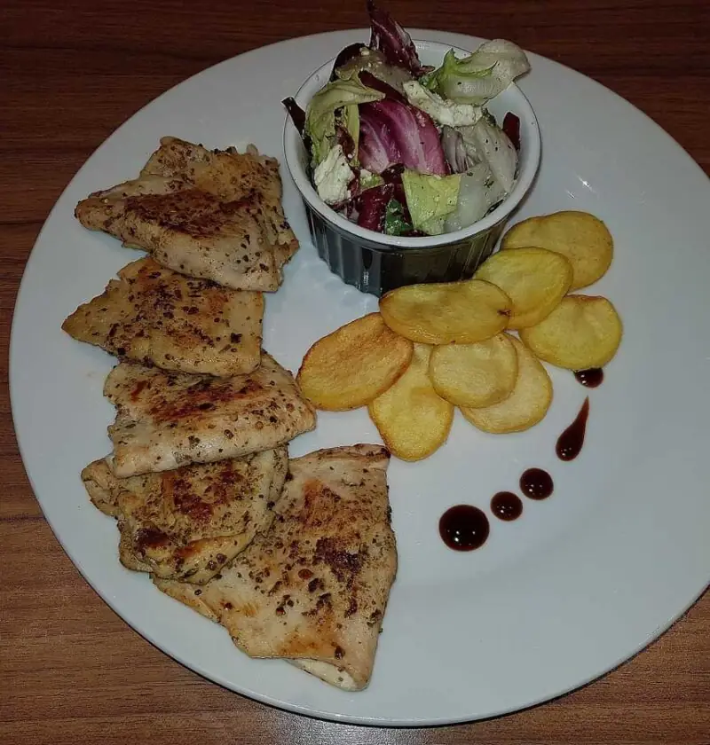 Gevulde kipschnitzel met feta, naast een salade en gefrituurde aardappelschijfjes.