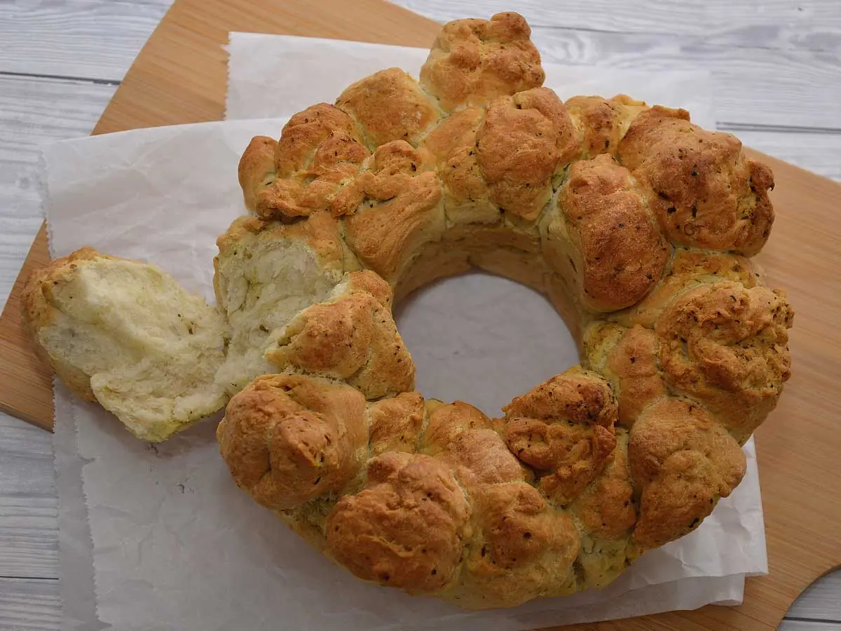 Een heerlijk zelf gebakken plukbrood met pesto, met een stuk eraf geplukt.