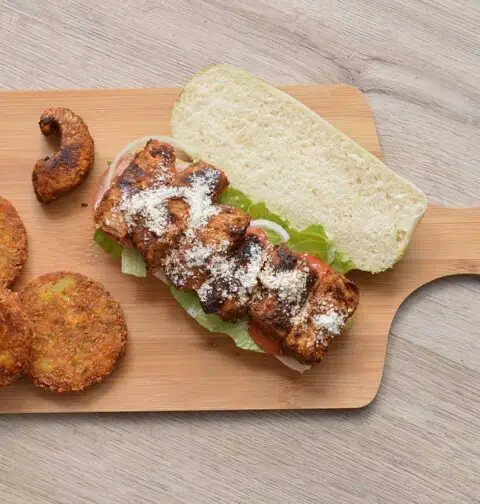 Een pesto broodje met gekruidekip op een snijplank.