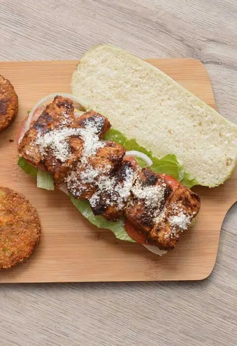 Een pesto broodje met gekruidekip op een snijplank.